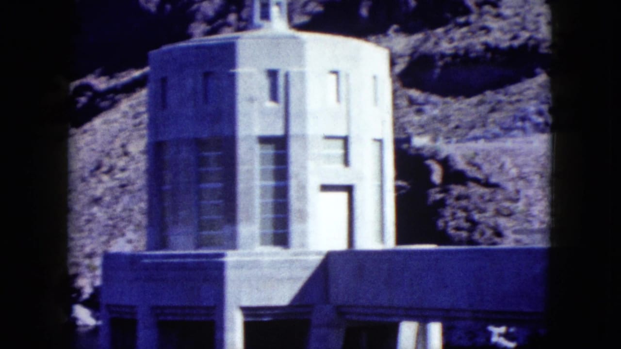 1959 Nevada 8mm frame showing a pale geometric stone tower and building facade set below rocky mountain terrain.