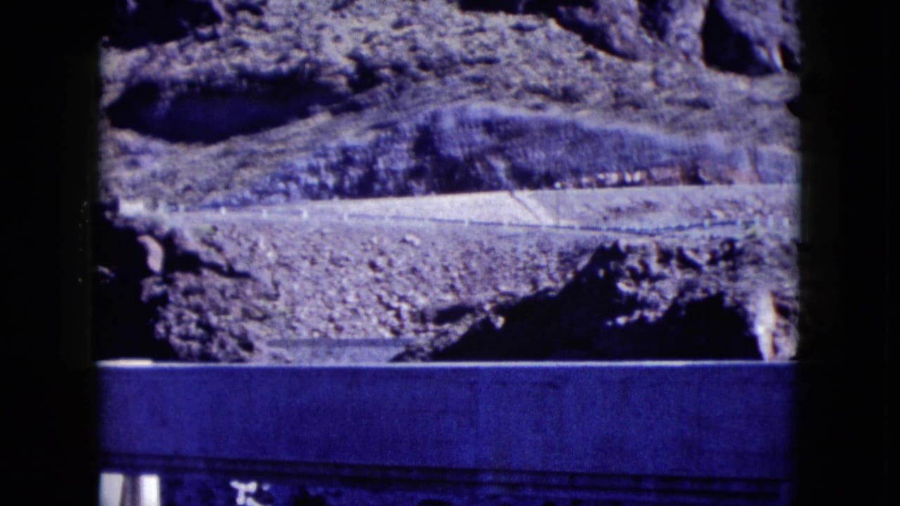 1959 Nevada home-movie frame with rocky terrain behind the upper portion of a pale stone building.