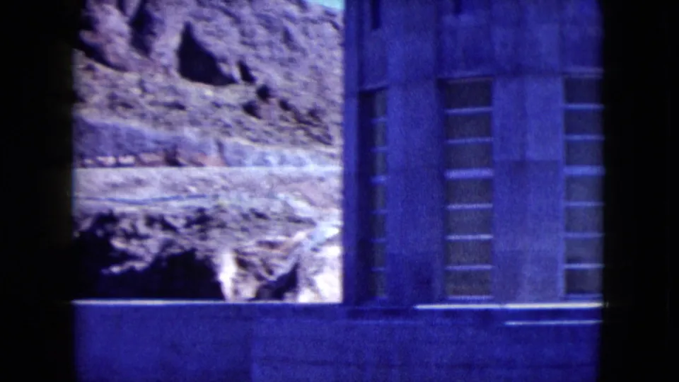 1959 Nevada 8mm view of the lower stone building facade, vertical window bands, and rough mountain ground.