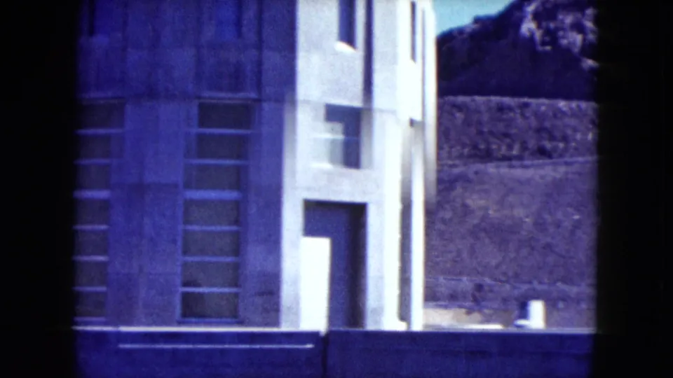 1959 Nevada frame showing the building's tower-like section, tall recessed windows, and mountain terrain in the background.