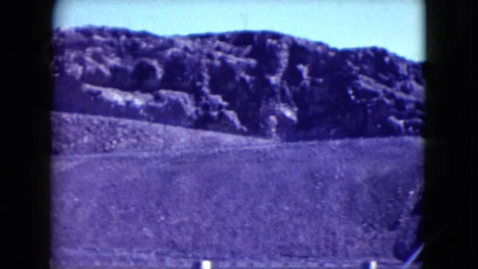 1959 Nevada 8mm view across a rocky desert hillside and open graded slope near an industrial site.