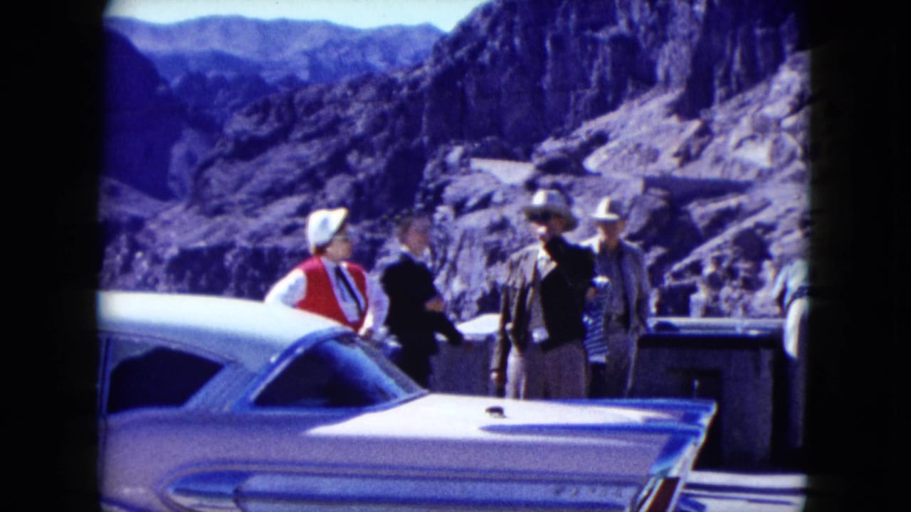 1959 Nevada frame with visitors, a possible uniformed official, and a white classic car at a dam overlook.