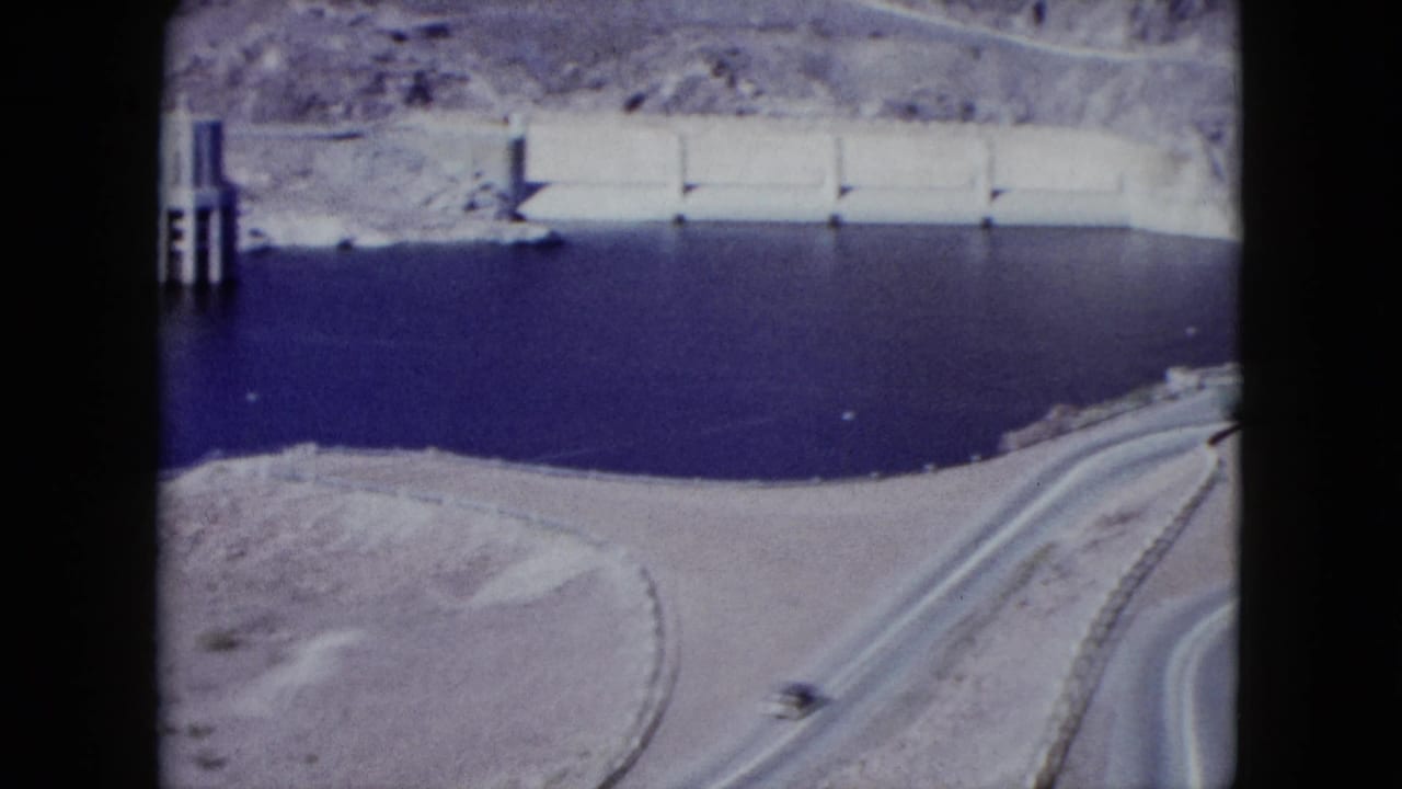 Reservoir water beside a concrete dam wall and curving desert road.