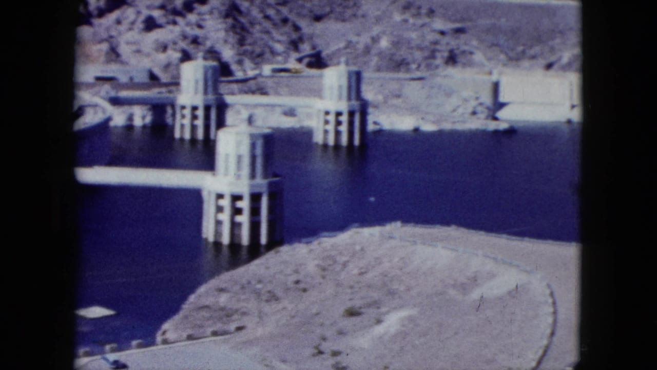 Concrete dam structures and intake towers rising from blue reservoir water.