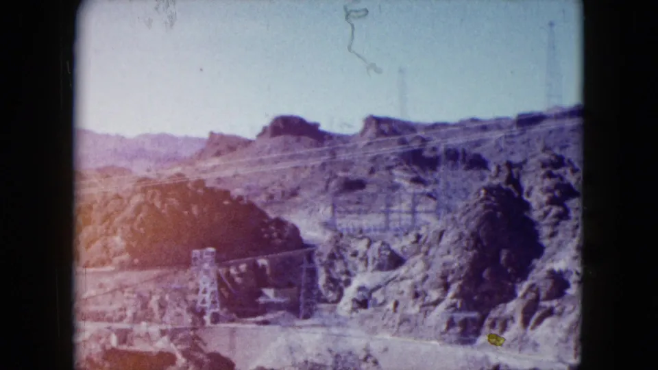 1959 Nevada frame showing the rocky landscape around Hoover Dam, with a road, canyon slopes, and part of the reservoir area.