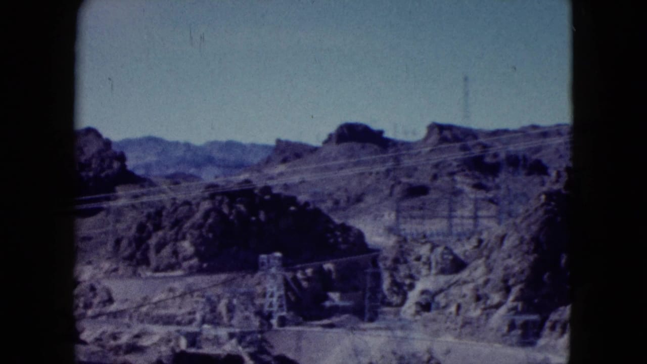 1959 Nevada 8mm frame showing rocky desert terrain crossed by power lines and small utility towers.