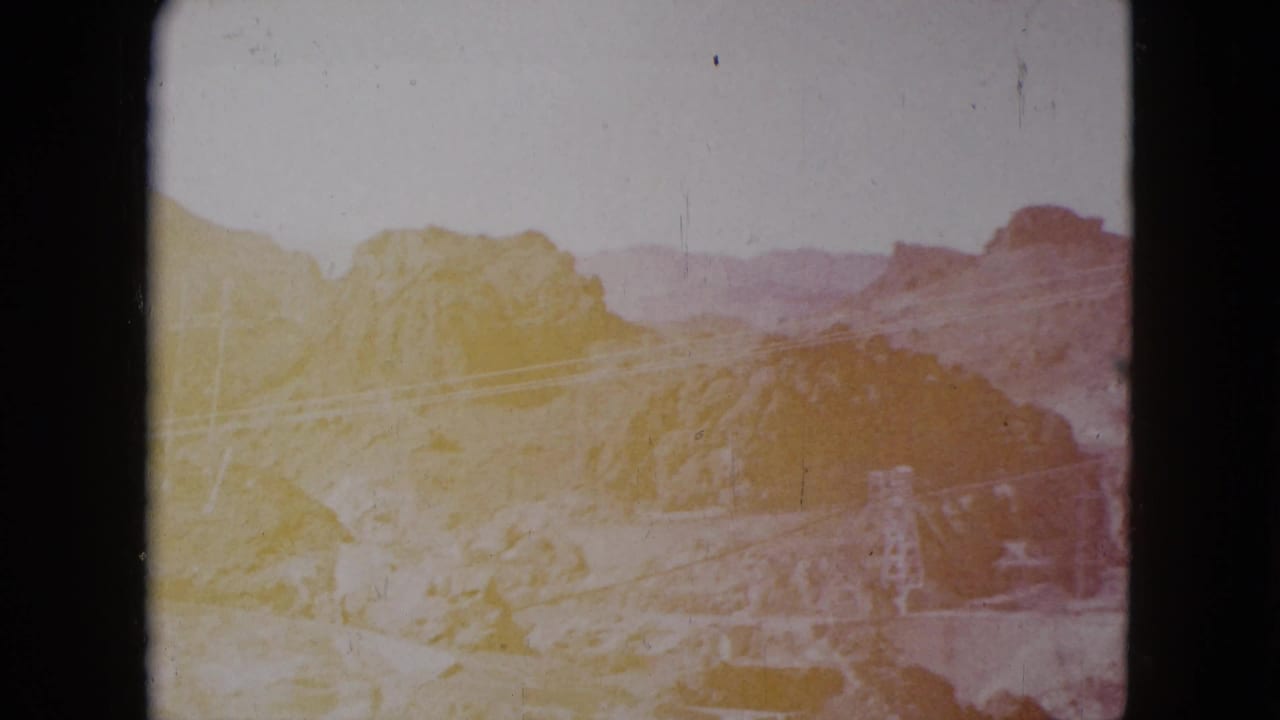 Faded 1959 Nevada desert view with rocky hills, distant ridges, and utility structures softened by exposure shift.