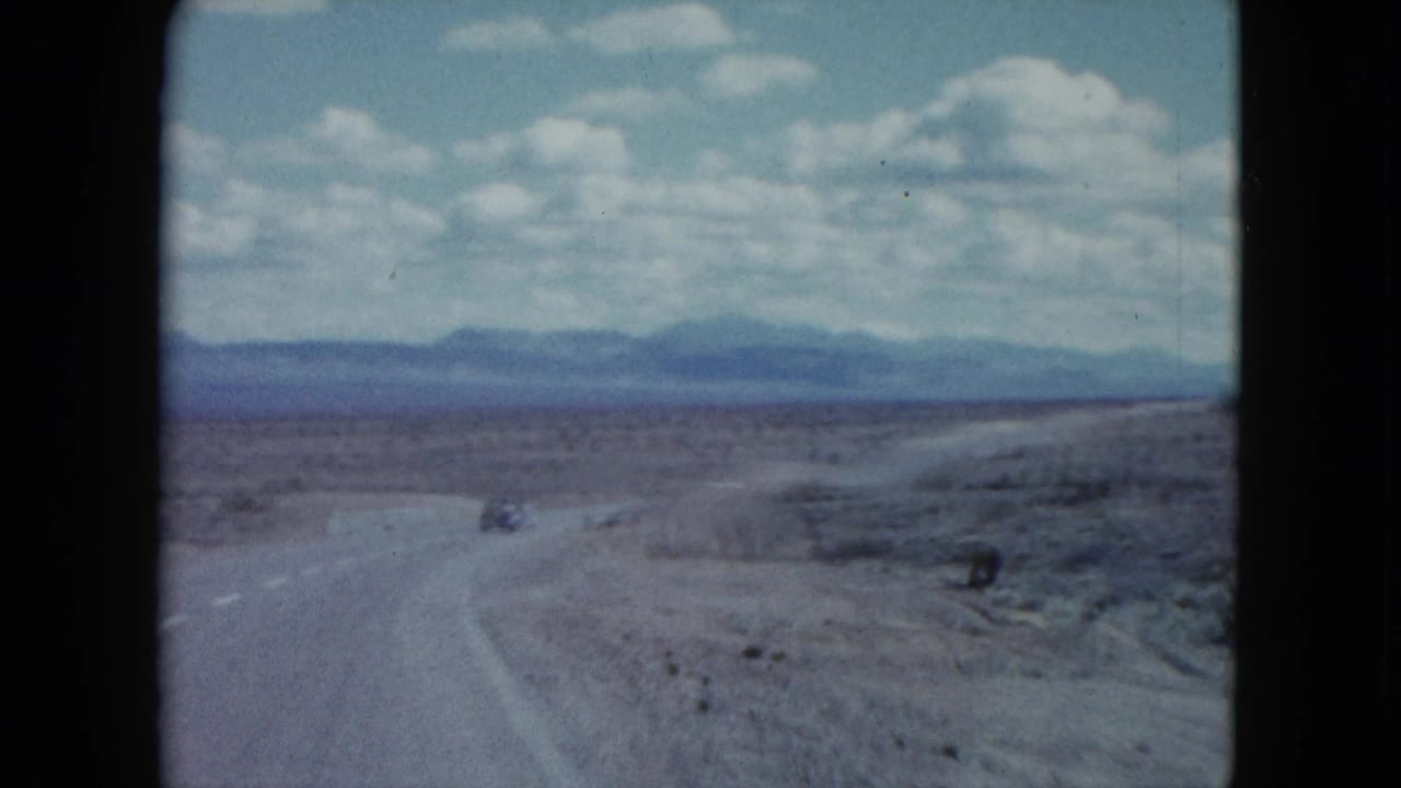 1959 Nevada road-trip view with a small car on a winding highway through open desert terrain.