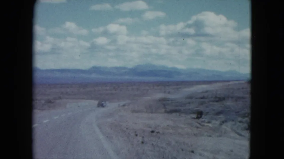 1959 Nevada road-trip view with a small car on a winding highway through open desert terrain.
