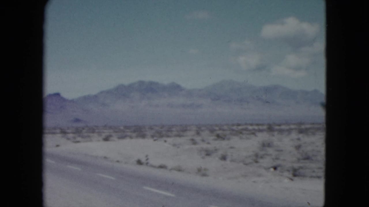 Nevada desert highway scene from 1959 footage, with sparse roadside vegetation, distant mountains, and no clearly visible people or structures.