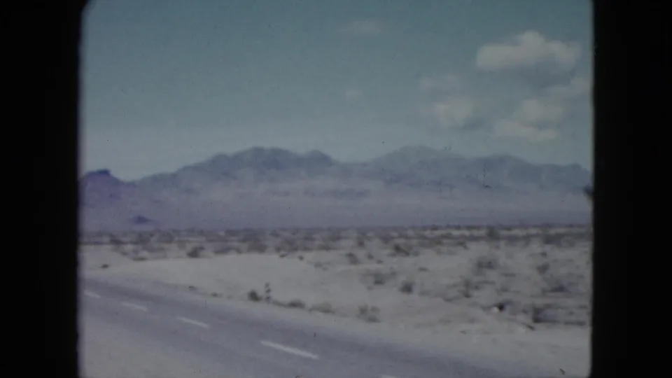 Nevada desert highway scene from 1959 footage, with sparse roadside vegetation, distant mountains, and no clearly visible people or structures.