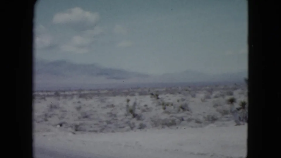 Nevada 1959 road-trip footage showing a broad desert plain, low vegetation, distant mountains, and rounded 8mm frame edges.
