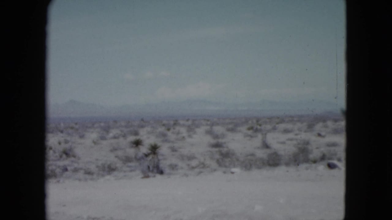 Vintage 8mm view of Nevada desert scrubland with a broad pale foreground and a low mountain horizon in the distance.