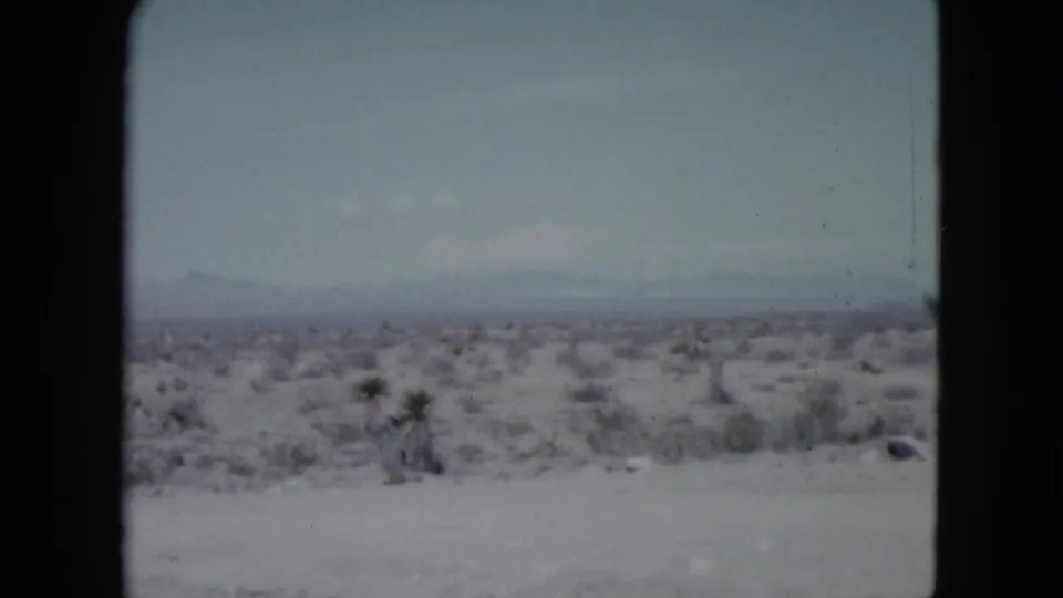 Vintage 8mm view of Nevada desert scrubland with a broad pale foreground and a low mountain horizon in the distance.