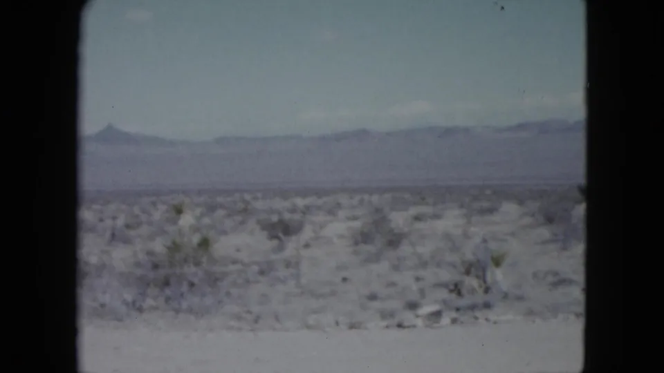 1959 Nevada 8mm frame showing open desert scrubland with a hazy mountain ridge in the distance.