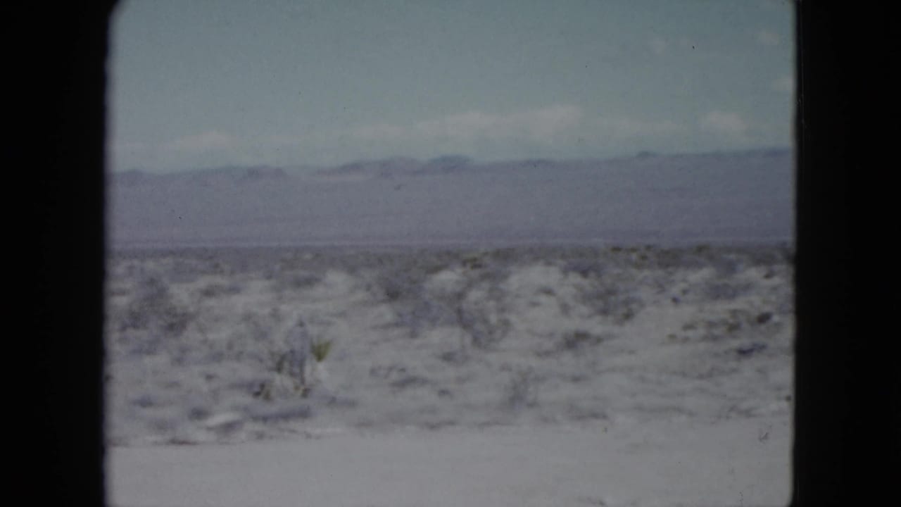 Nevada home-movie frame from 1959 with scrub-covered desert foreground and low mountains beyond.