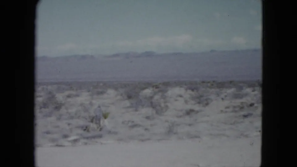 Nevada home-movie frame from 1959 with scrub-covered desert foreground and low mountains beyond.