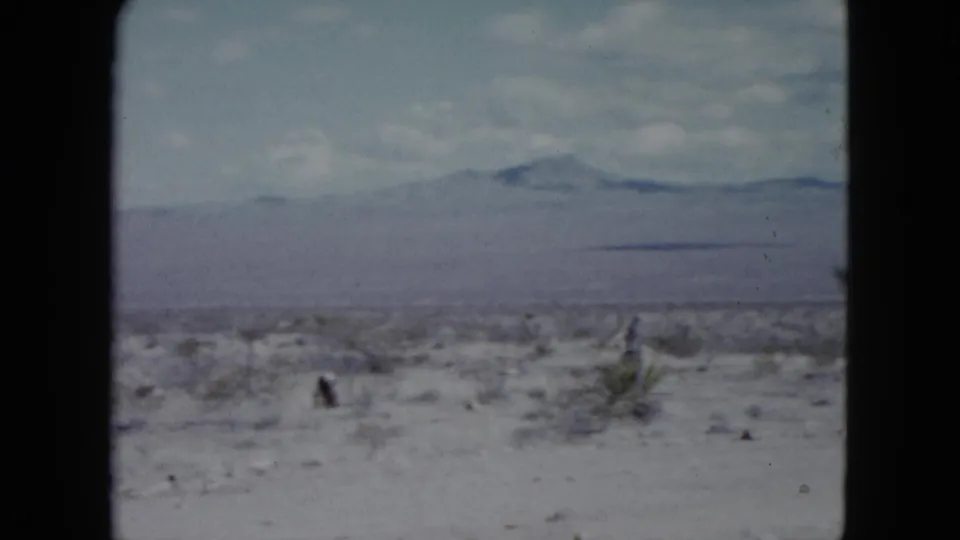 Nevada 8mm frame from 1959 showing arid scrubland, distant mountains, and a taller desert plant near the right edge.