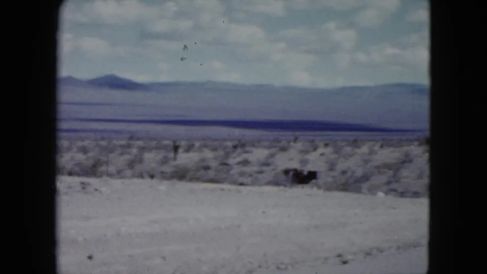 1959 Nevada 8mm view across dry ground and scrub toward distant mountains, with a darker horizontal strip across the landscape.
