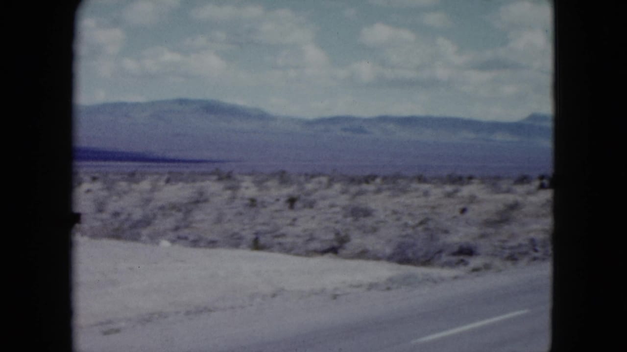 Two-lane desert highway curving past scrubland toward distant mountains.
