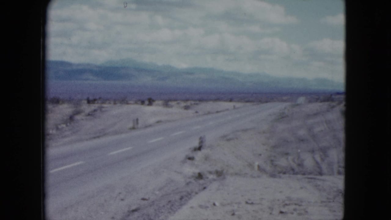 1959 Nevada home-movie view down a rural desert highway toward distant mountains under a bright sky.