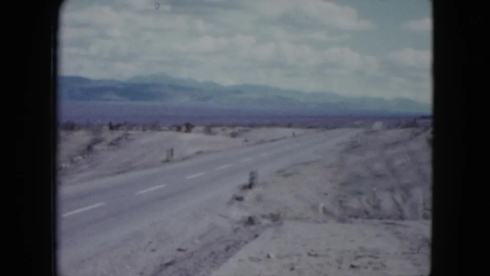 1959 Nevada home-movie view down a rural desert highway toward distant mountains under a bright sky.