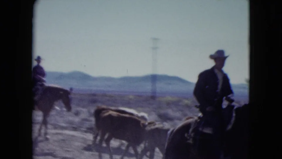 1959 Nevada 8mm frame showing horseback riders in cowboy hats with cattle in a dry open landscape and distant hills.