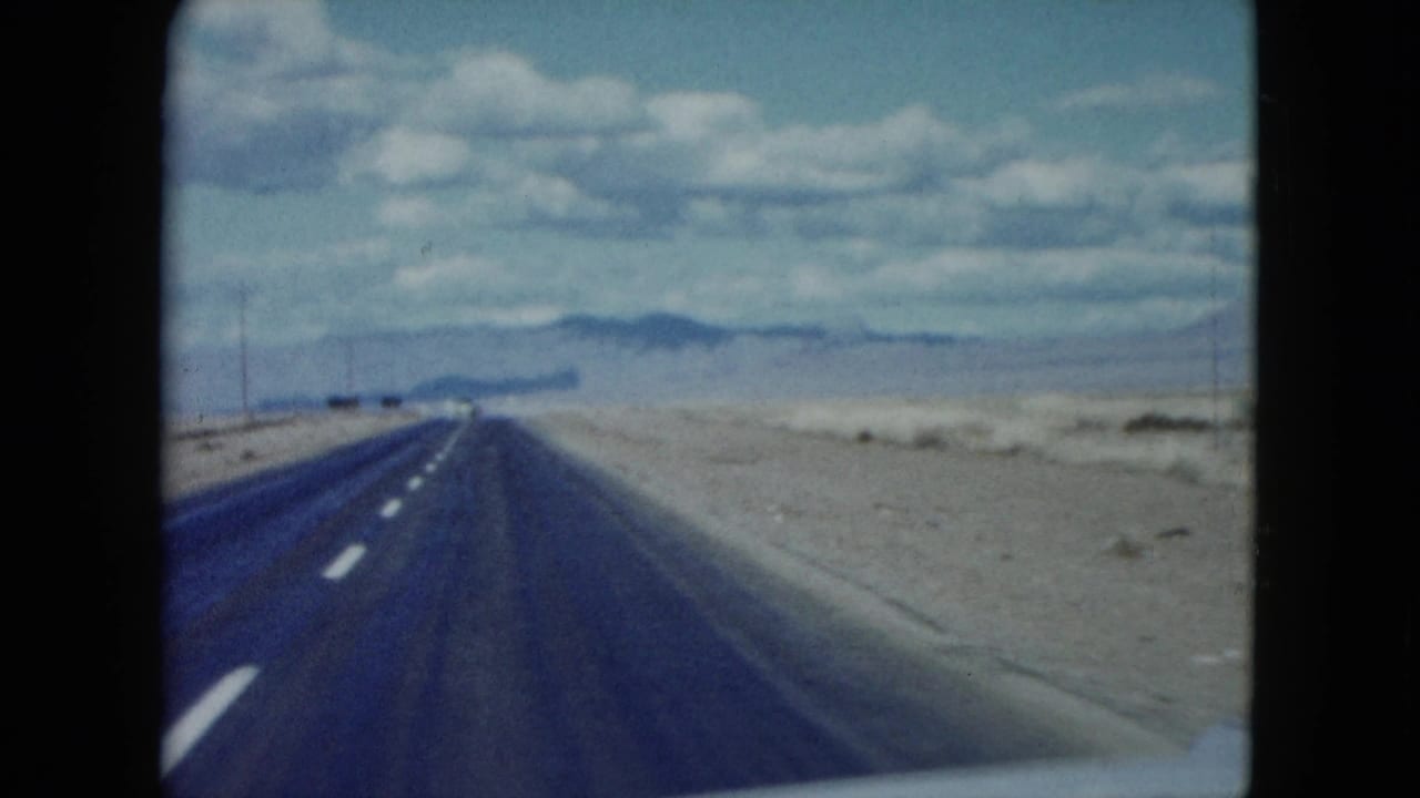 Straight desert highway stretching toward distant mountains beneath scattered clouds.