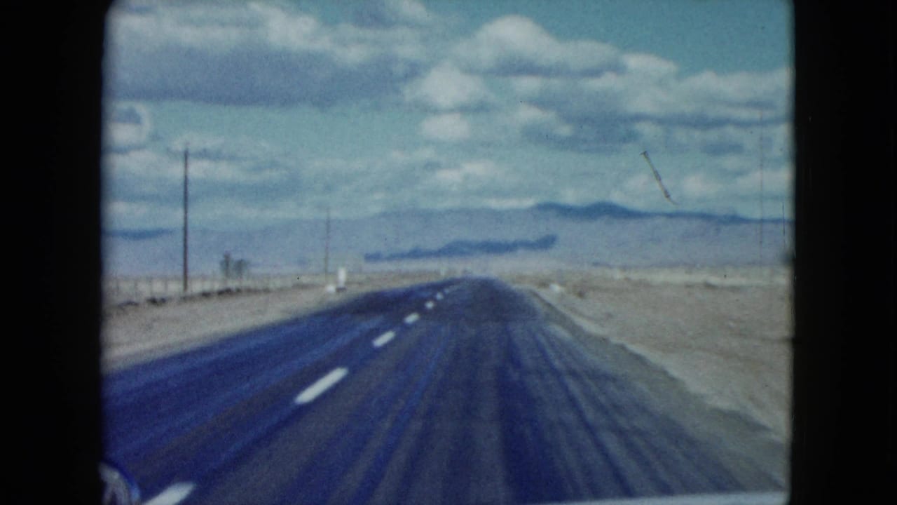 Passenger-view 1959 Nevada footage shows an empty two-lane highway running through dry open terrain toward distant hills.