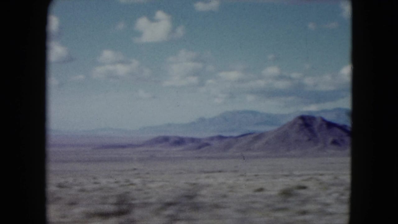 Distant desert mountains and scrubland under a blue sky with small clouds.