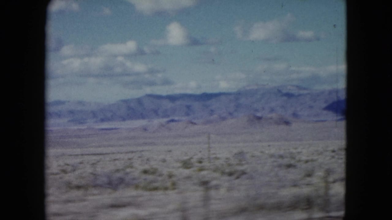Open desert plain with mountains and clouds framed by dark film borders.