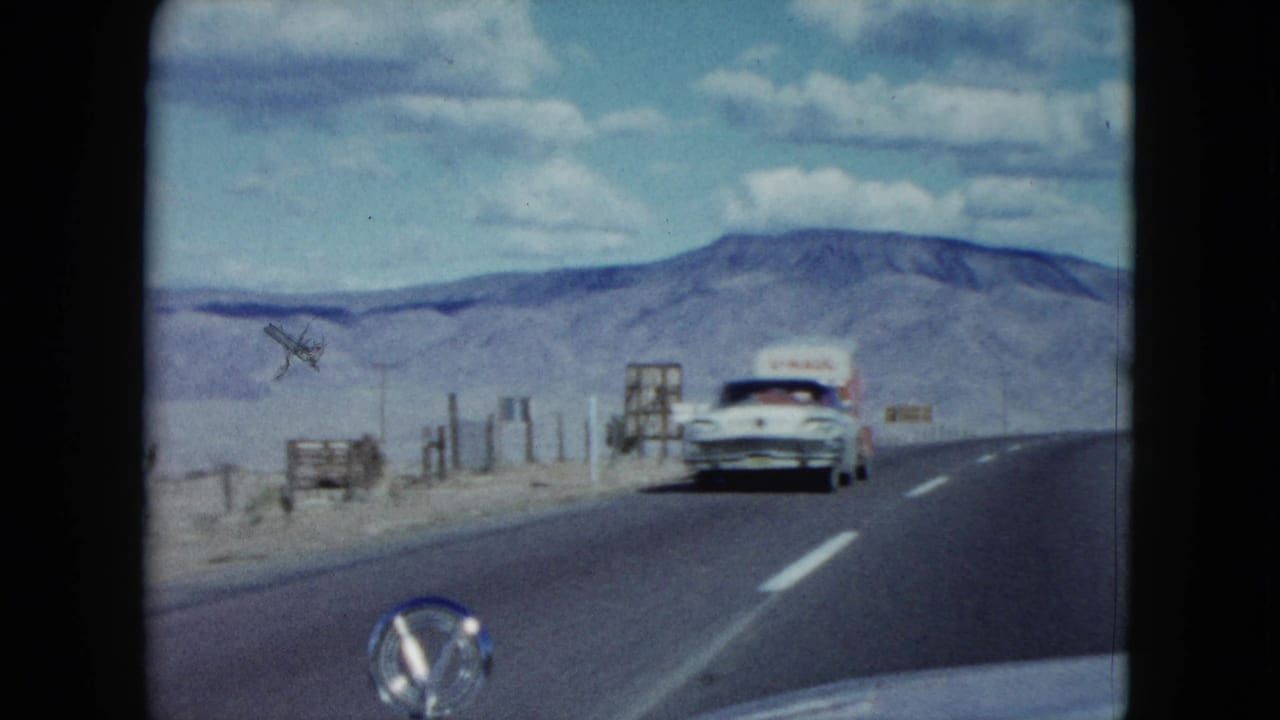 1959 Nevada desert highway view from a moving car as a classic sedan approaches under a clouded blue sky.