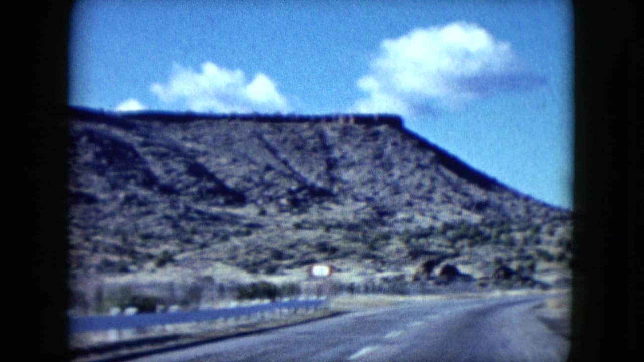 Curving paved road with desert hills and a small roadside structure ahead.