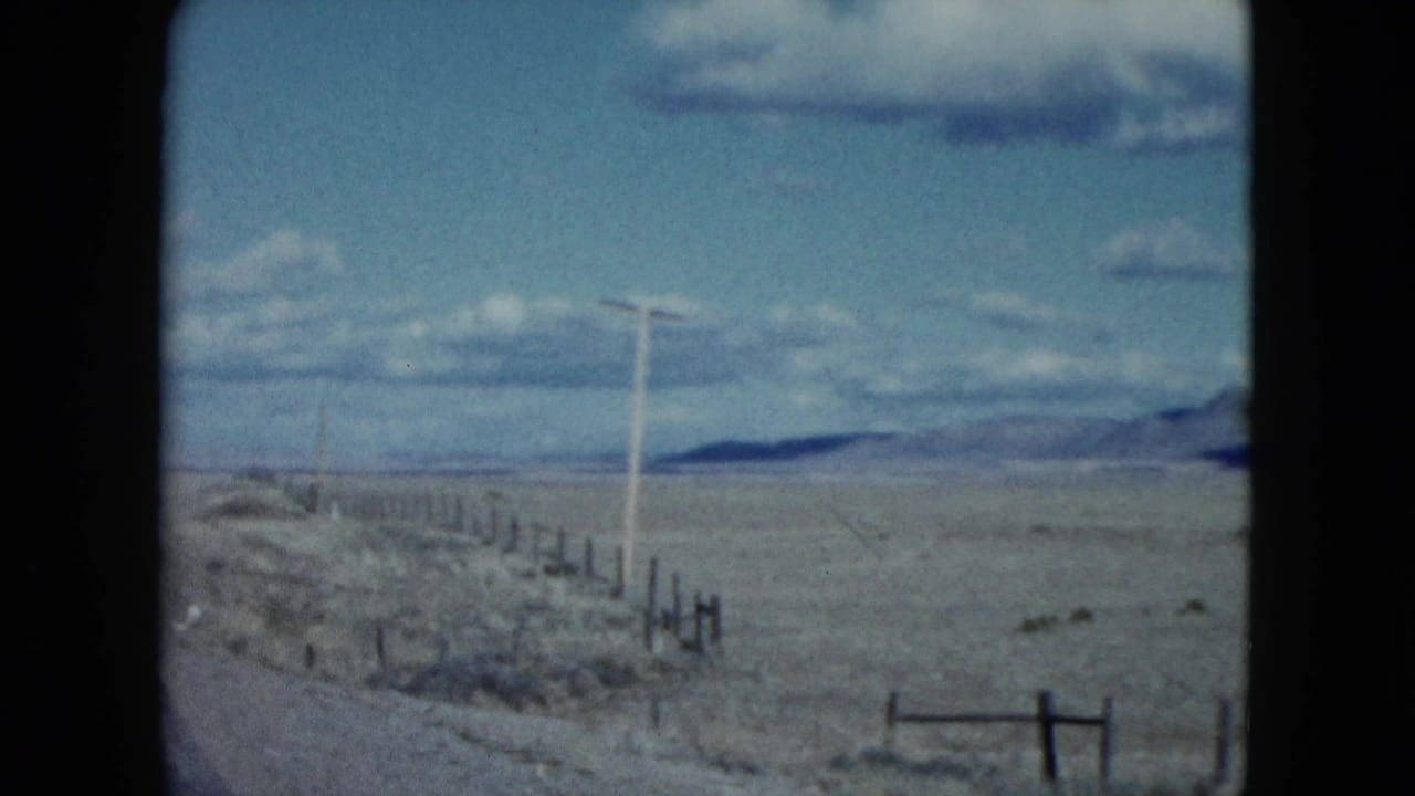 Roadside fence and utility poles cross an open desert plain with mountains beyond.