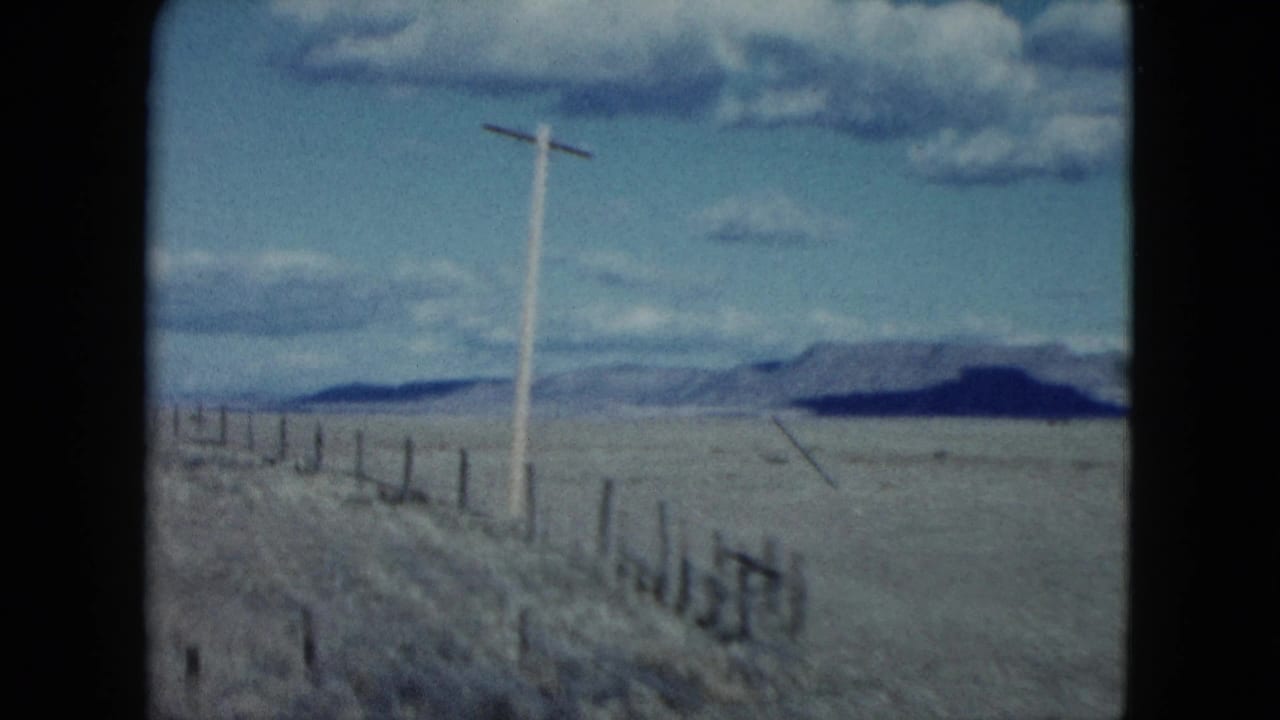 1959 Nevada 8mm travel frame looking past a roadside utility pole and fence toward open desert mountains.