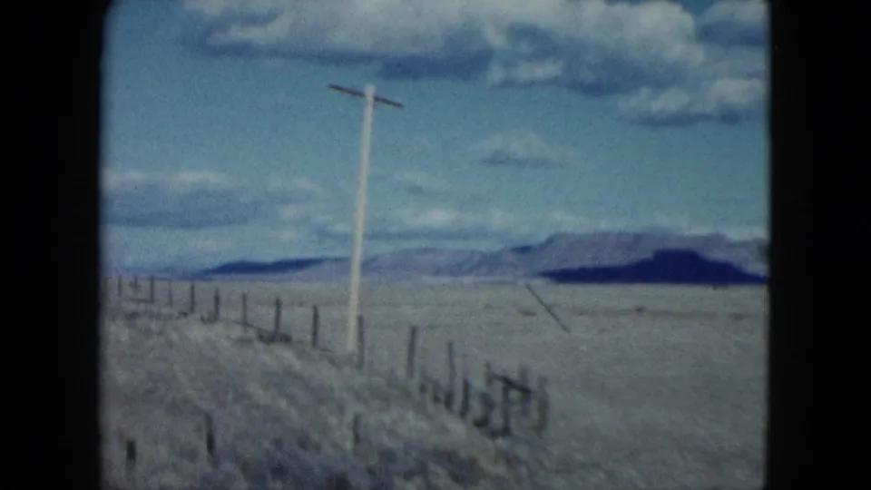 1959 Nevada 8mm travel frame looking past a roadside utility pole and fence toward open desert mountains.
