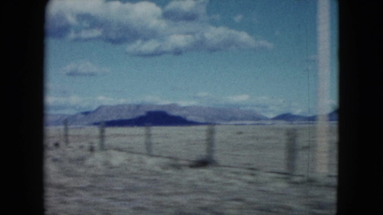 1959 Nevada home-movie frame showing a fence line across flat desert terrain with mountains on the horizon.