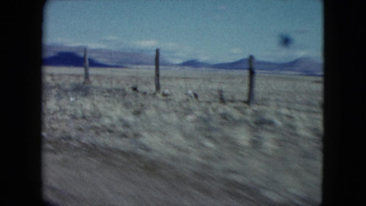 1959 Nevada 8mm frame showing a blurred desert roadside with wooden fence posts, low mountains, and open blue sky.
