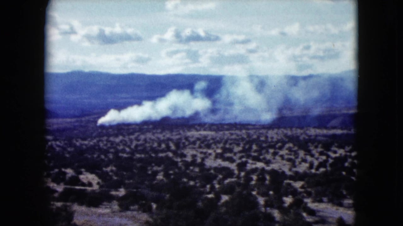 1959 Nevada 8mm frame showing white smoke spreading over scrub desert beneath distant mountains and a bright sky.