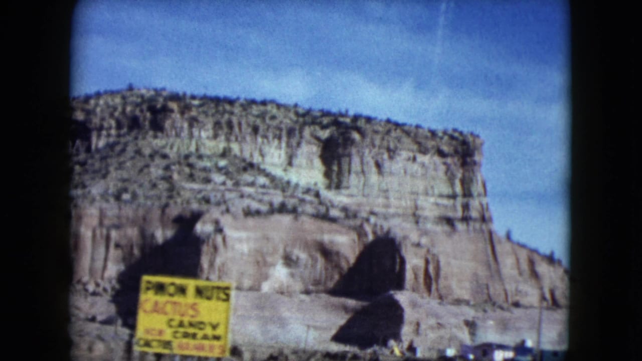 1959 Nevada road-trip frame with a rocky mesa behind a yellow sign reading pecan nuts, cactus candy, and ice cream.