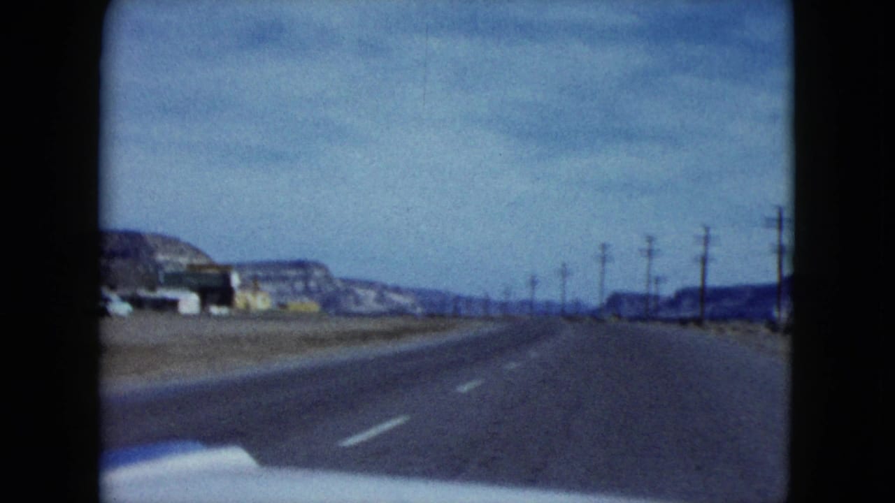 Two-lane desert highway with utility poles and distant mesas seen from a moving car.