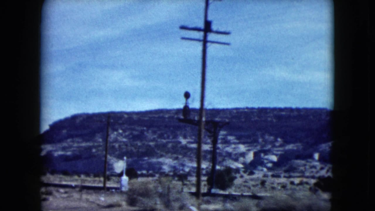 1959 Nevada home-movie frame from a moving road view, with utility poles in front of distant desert canyon ridges.