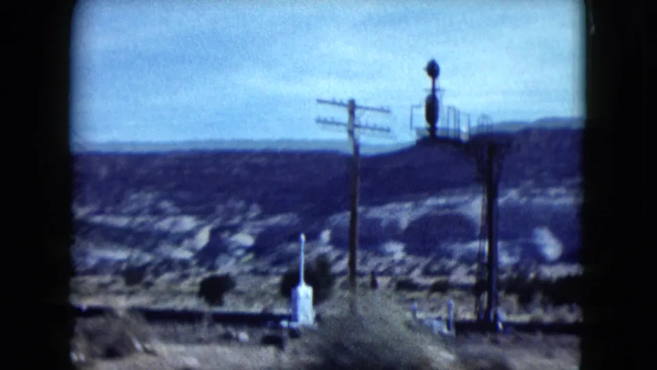 Nevada desert road scene with utility poles, a pale roadside marker, scrub, and canyon hills in the distance.