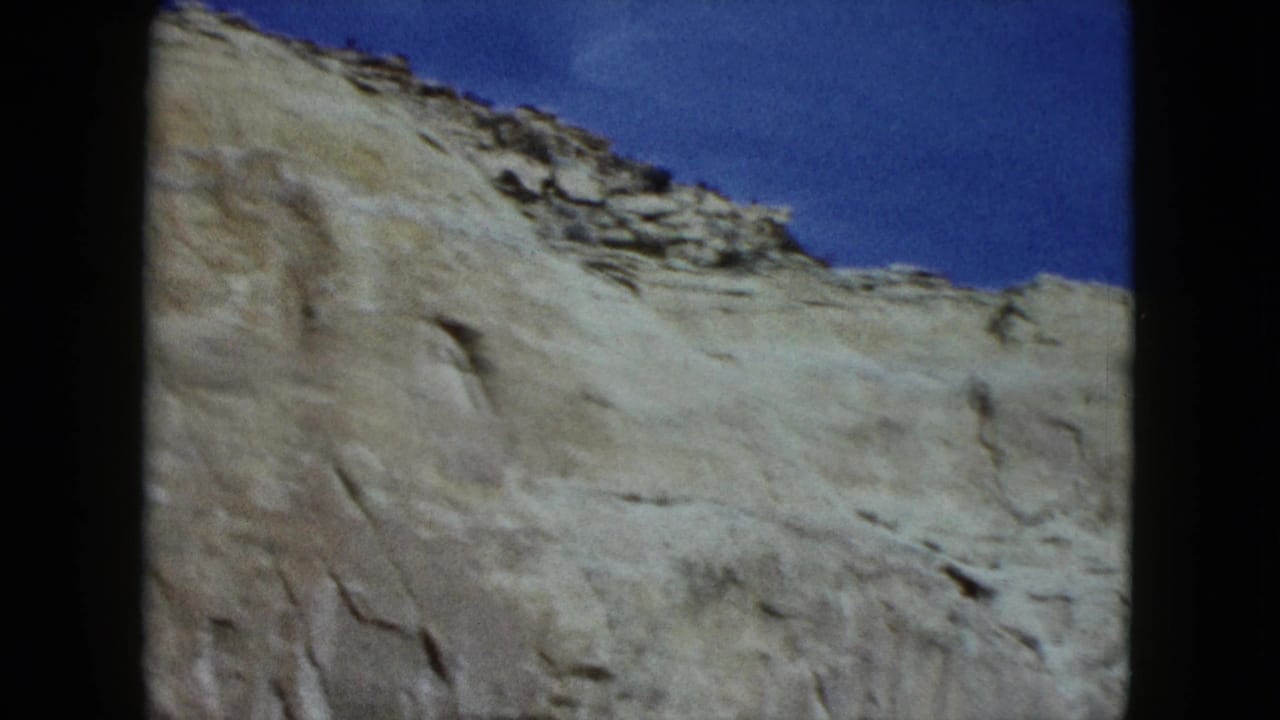 Close passing view of pale rock wall beneath a blue sky.