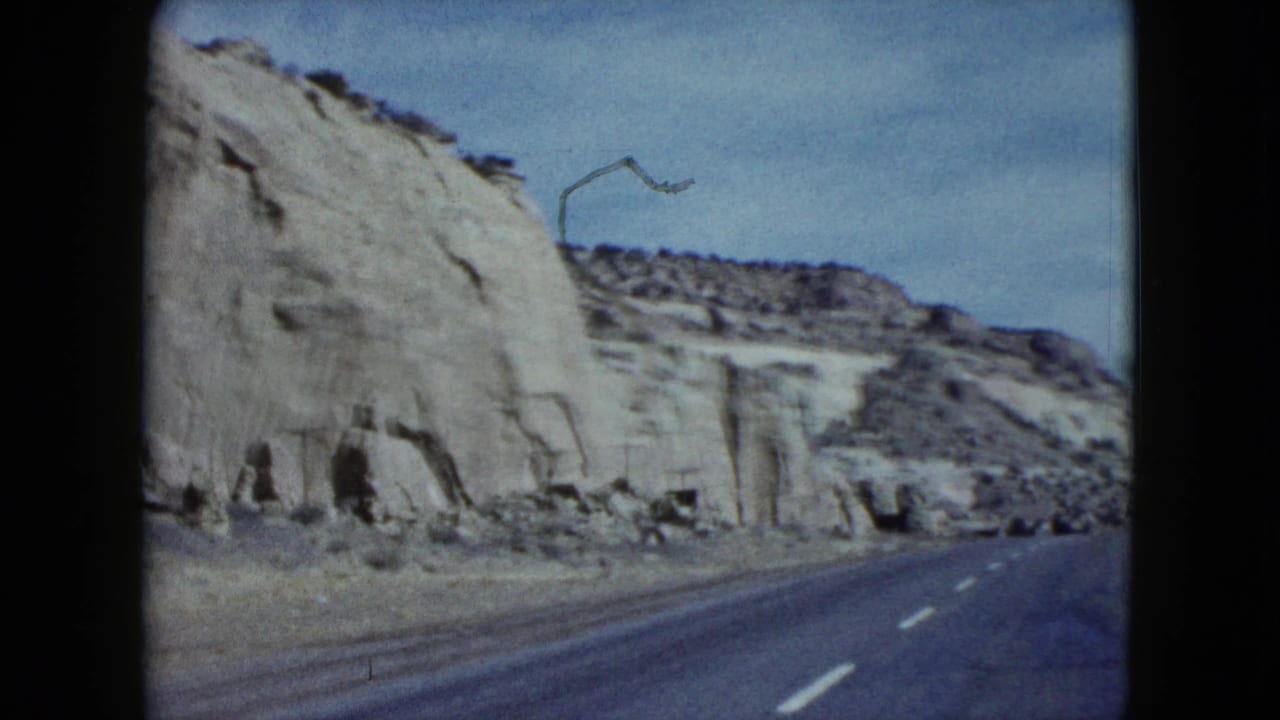 Two-lane road curves past pale desert cliffs with utility poles nearby.
