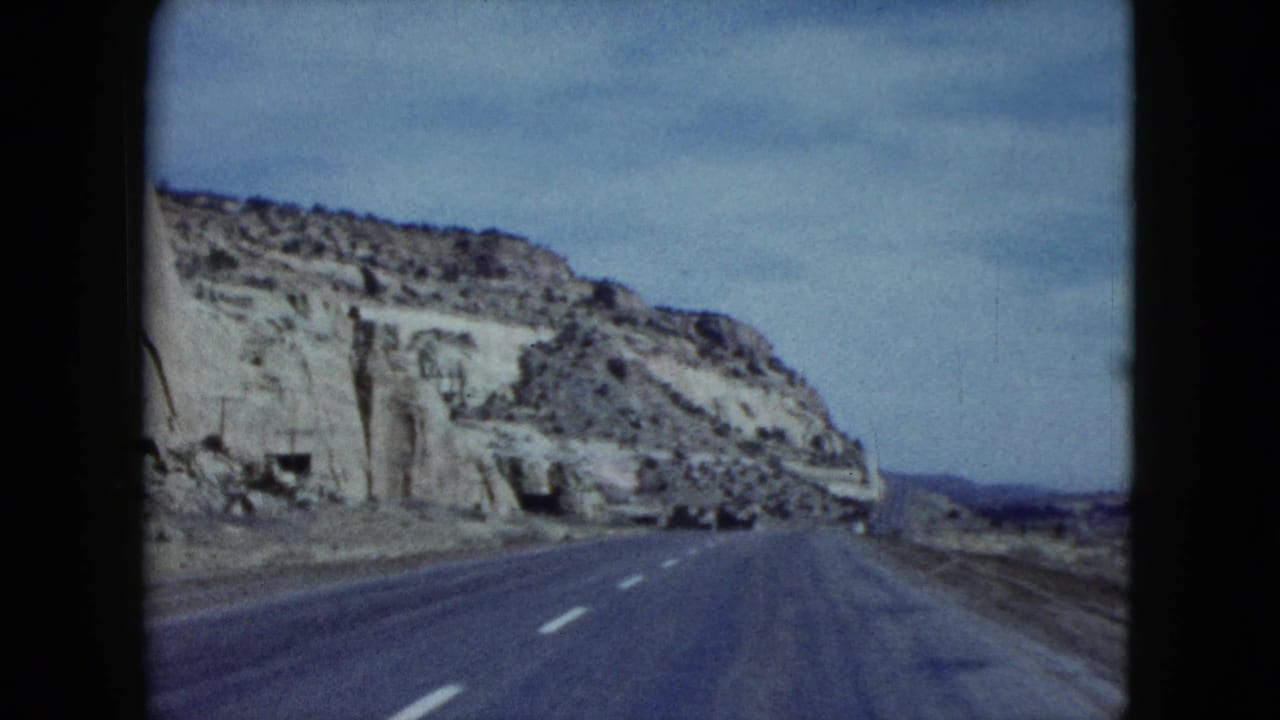 1959 Nevada 8mm frame showing a paved highway extending beside eroded cliffs toward distant arid land.
