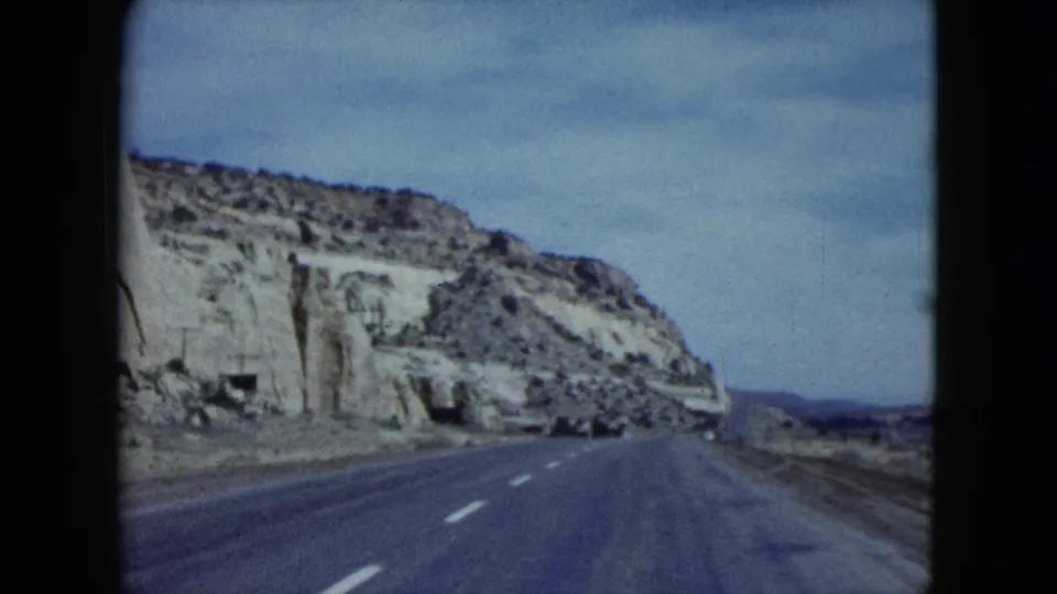 1959 Nevada 8mm frame showing a paved highway extending beside eroded cliffs toward distant arid land.