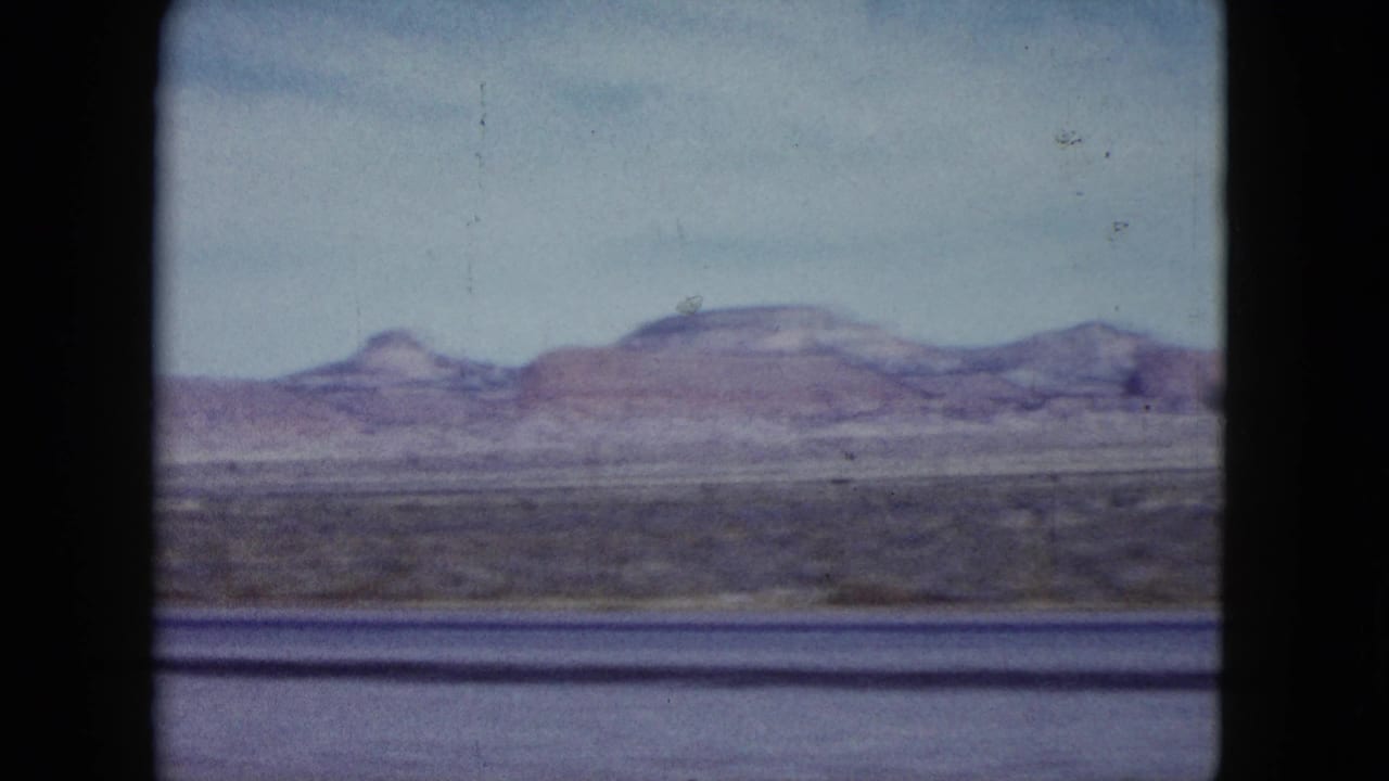 Open desert foreground with low mountains and mesas beneath a hazy sky.