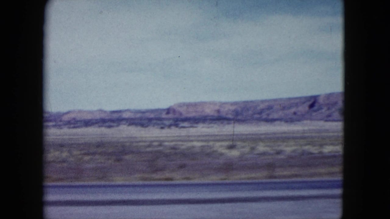 Open desert landscape with low mountains and window framing from a moving vehicle.