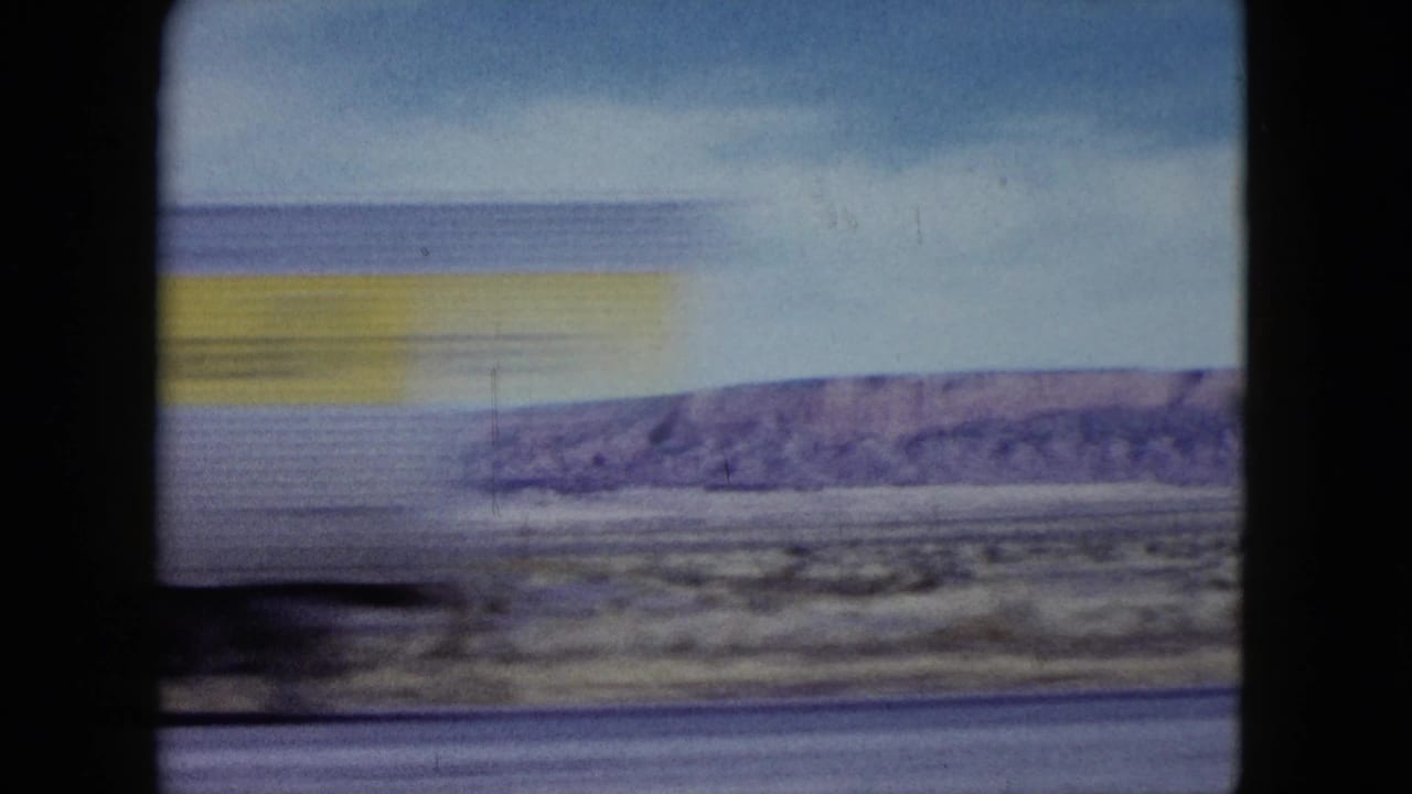 A yellow-and-white truck or bus appears blurred near the left of a Nevada desert view, with hills and roadside visible beyond.